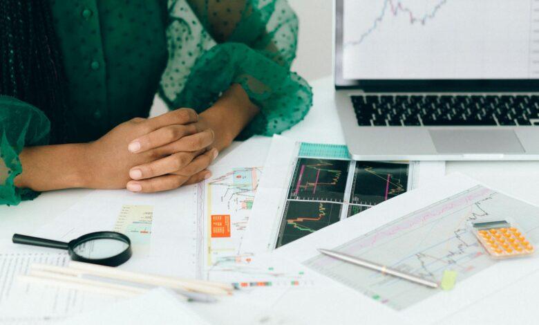 A person analyzes financial charts and graphs at a desk, indicating business trading activity.